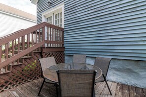 Une terrasse en bois avec une table ronde et des chaises, un escalier en bois et une maison à l’extérieur bleu.