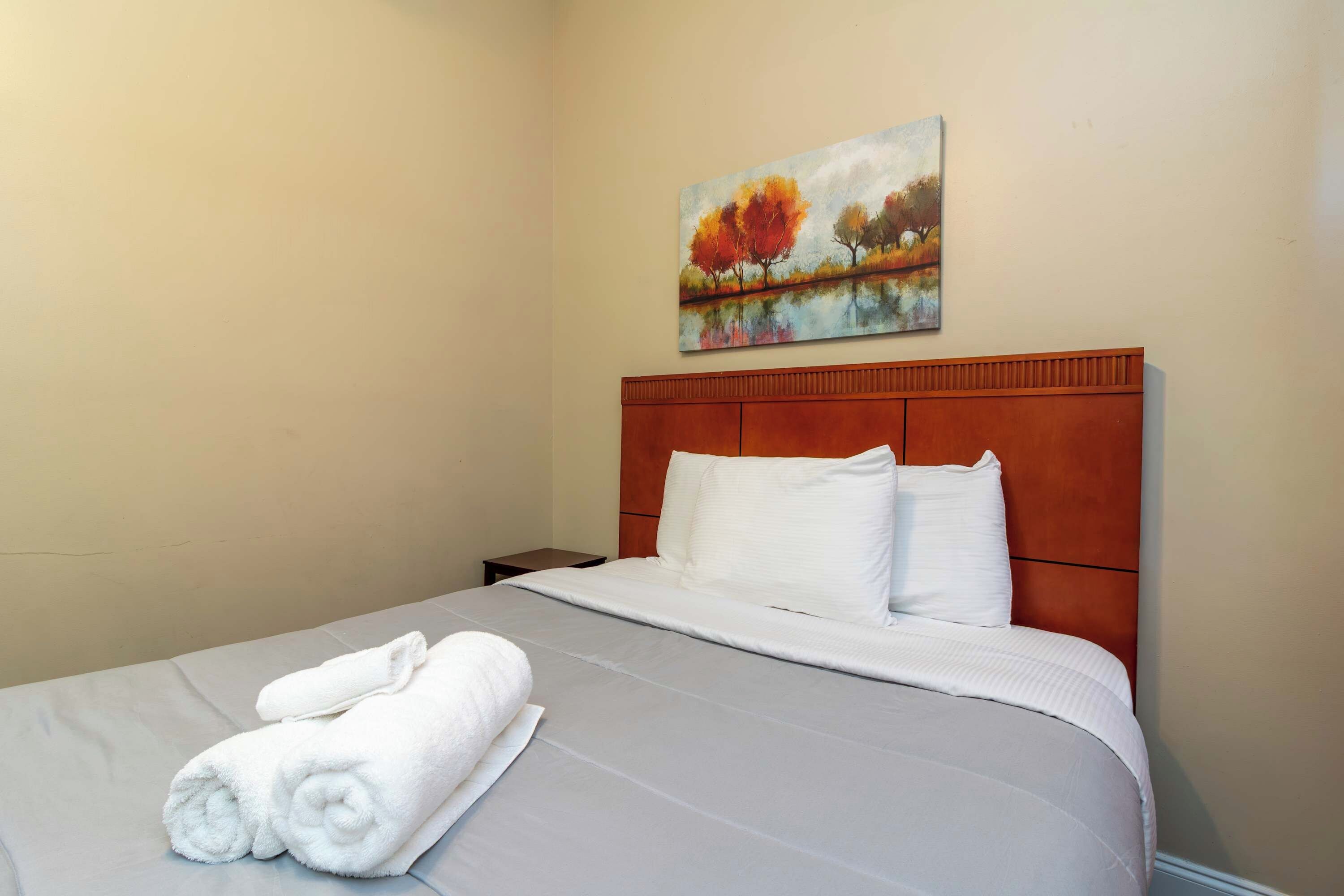 Quarto de hotel com cama, pintura de árvores de outono e cama bem arrumada com toalhas.