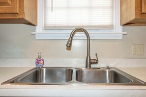 A kitchen with a double stainless steel sink, a faucet, and a soap dispenser. - Closest Historic BnB to Ft Moore-Americana Cottage (Columbus)