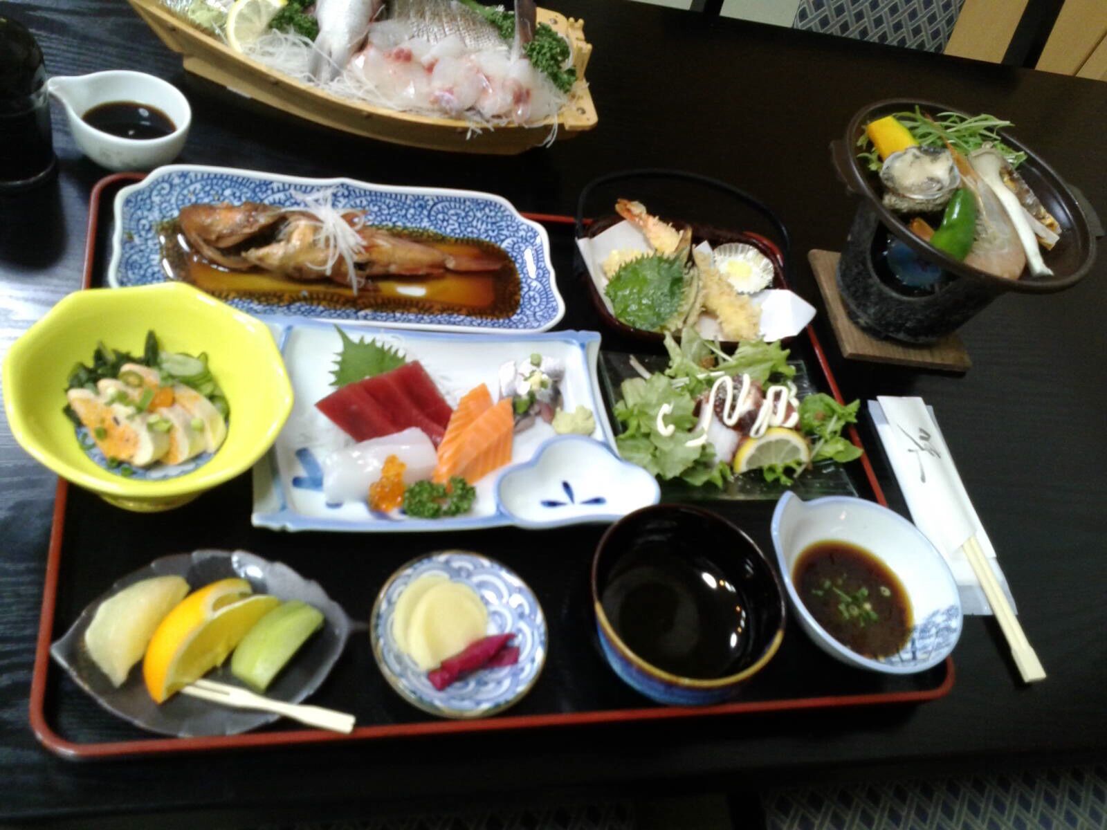 A tray with various Japanese dishes, including sashimi, sushi, and a salad.
