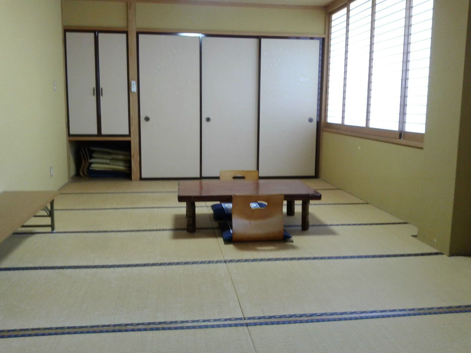 Una habitación con esteras de tatami, una mesa baja y sillas, puertas correderas y un ventanal.