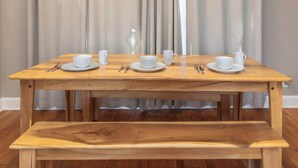 Une table en bois, des tasses et des soucoupes blanches, un banc et un rideau en arrière-plan.