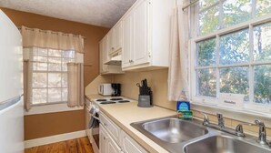 Une cuisine compacte équipée d’un four à micro-ondes, d’une cuisinière, d’un évier et d’une fenêtre donnant sur les arbres.