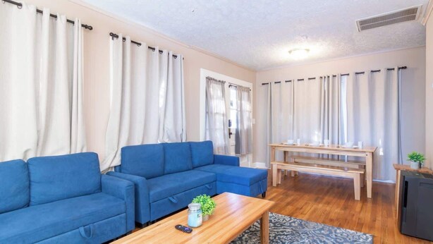 Un salon avec un canapé bleu, une table basse en bois, un tapis à motifs et une petite table sur laquelle se trouvent des tasses et une plante.