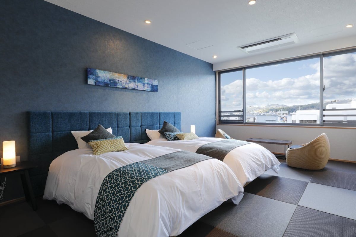 Une chambre d’hôtel moderne avec un grand lit, une vue sur la ville et un mur d’accent bleu.