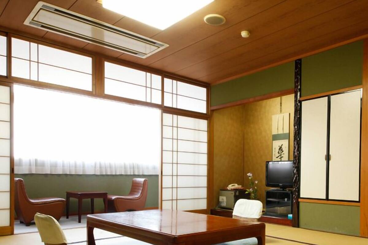Une pièce avec un sol recouvert de tatamis, une petite table, des chaises et un téléviseur japonais traditionnel.