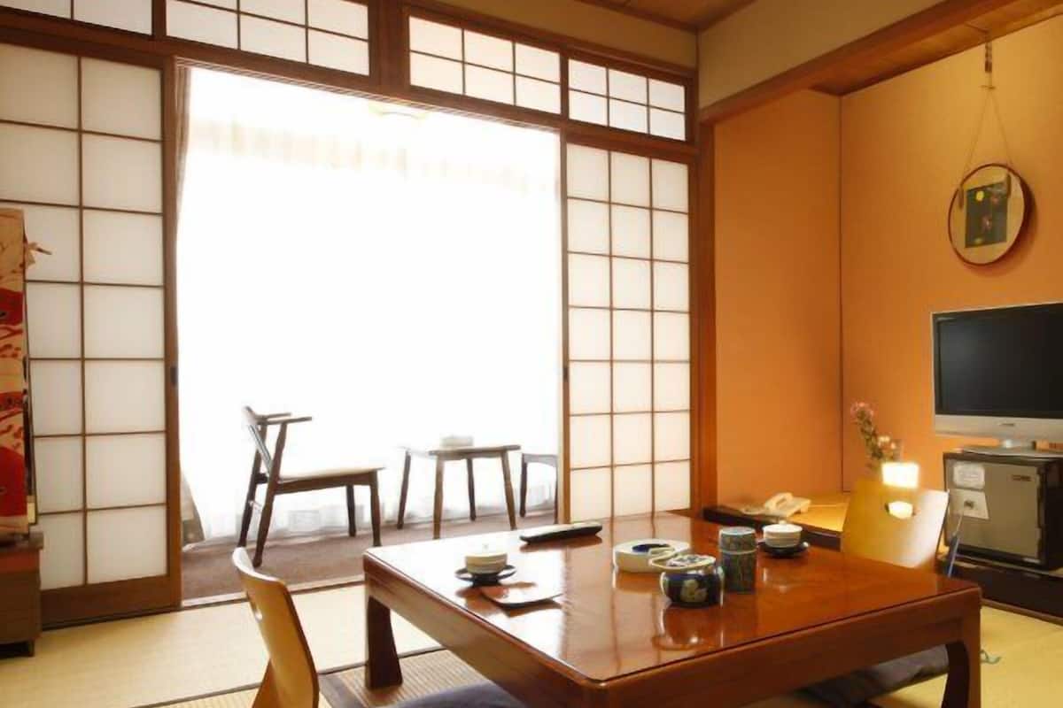 Une pièce de style japonais traditionnel, avec un sol recouvert de tatamis, une petite table en bois, un téléviseur et une porte coulissante.