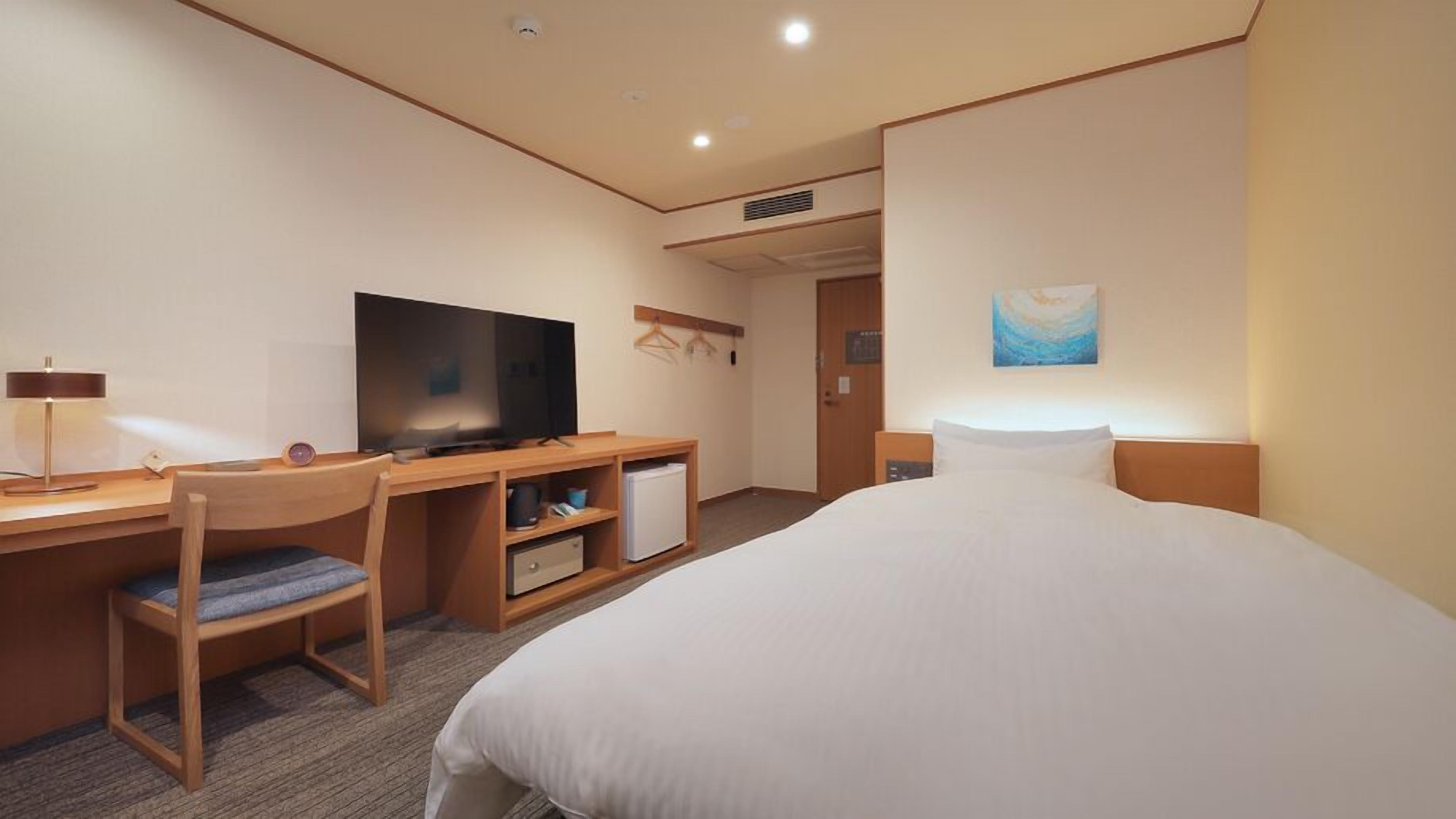 A hotel room with a bed, desk, chair, television, and a small refrigerator.