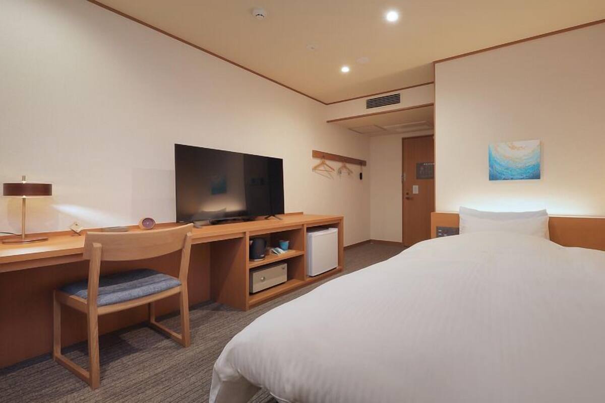 Une chambre d’hôtel équipée d’un lit, d’un bureau, d’une chaise, d’une télévision et d’un petit réfrigérateur.