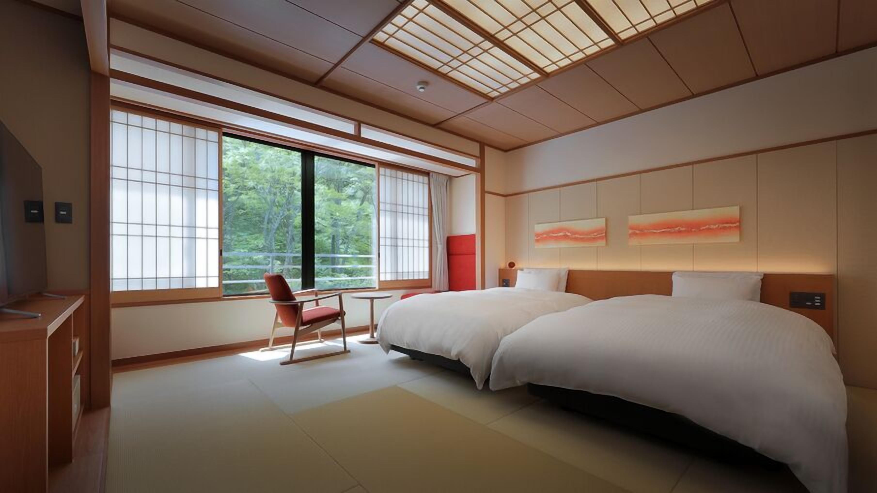 A modern hotel room with two beds, large windows, a red chair, and artwork on the wall.