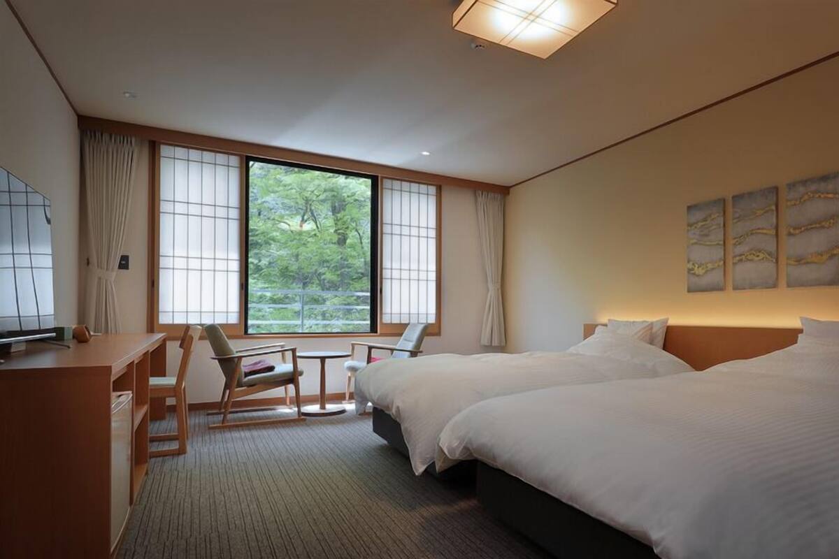 Une chambre d’hôtel avec deux lits, un bureau, une chaise et une vue sur la verdure.