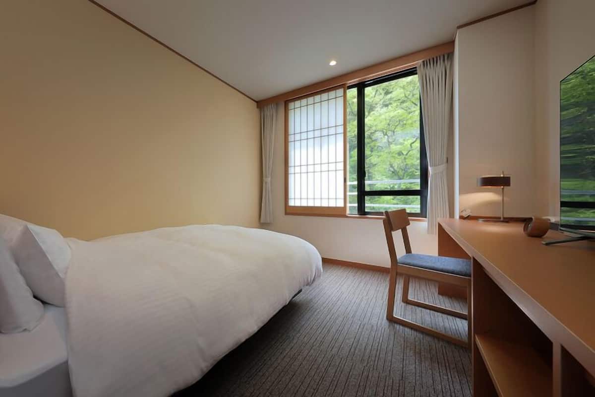 Une chambre d’hôtel avec un lit, un bureau, une chaise, une fenêtre avec des rideaux et une vue sur la verdure.