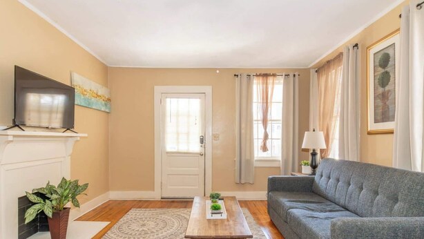 A living room with a grey sofa, a wooden coffee table, a television on a mantelpiece, a door with a window, and a patterned rug. - Downtown, Mins to Lakebottom Park-Our Midtown Nook (Columbus)