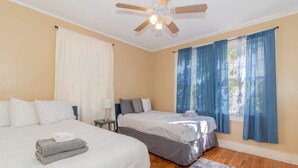 A hotel room with two beds, a ceiling fan, and large windows with blue curtains. - Downtown, Mins to Lakebottom Park-Our Midtown Nook (Columbus)