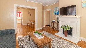 A living room with a fireplace, a television, and a dining area with a table and chairs. - Downtown, Mins to Lakebottom Park-Our Midtown Nook (Columbus)