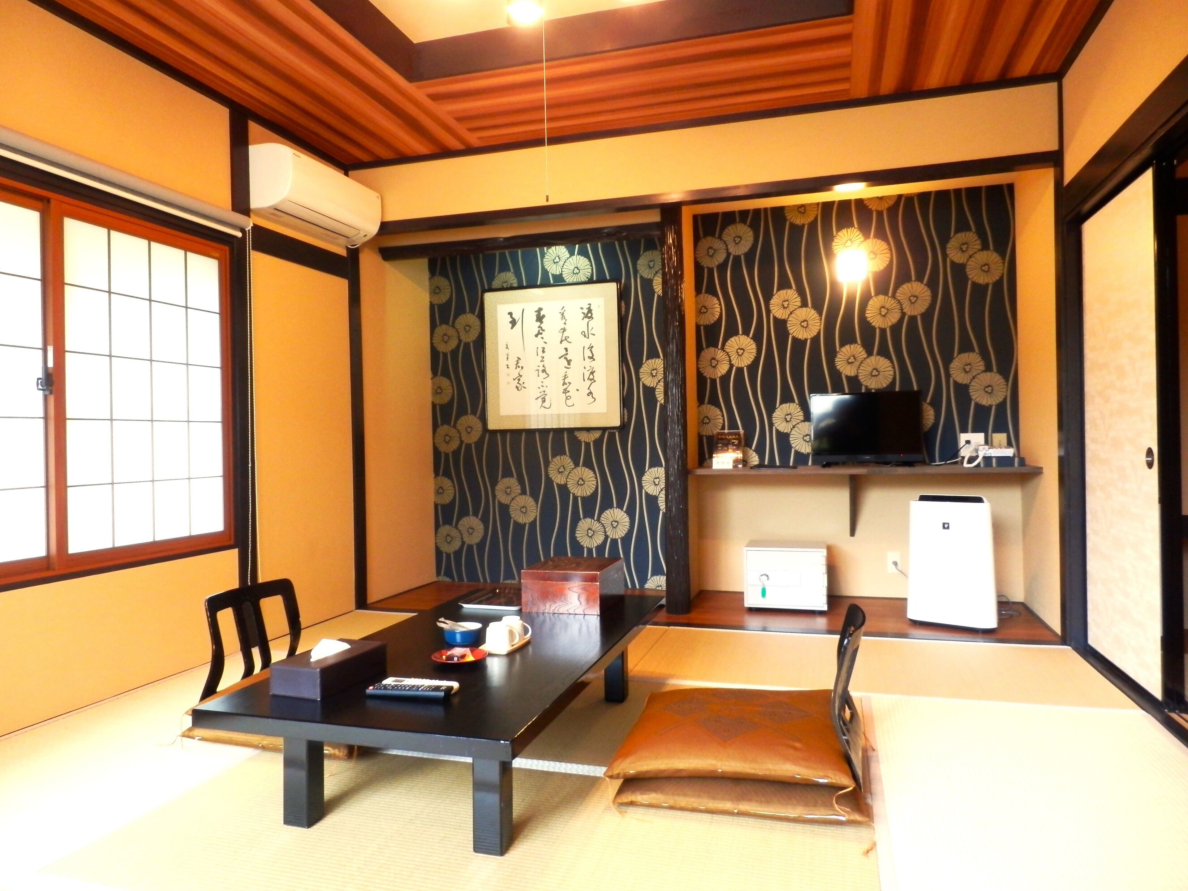A traditional Japanese room with tatami flooring, a low table with a remote control, a television, and a small refrigerator.
