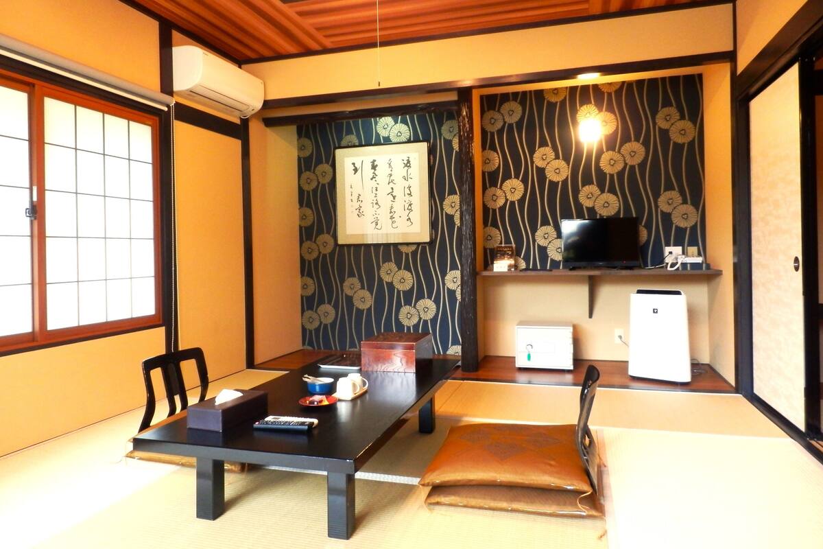 Ett traditionellt japanskt rum med tatamimattor på golvet, ett lågt bord med en fjärrkontroll, en tv och ett litet kylskåp.