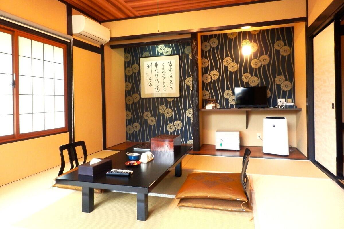 Ett traditionellt japanskt rum med tatamimattor på golvet, ett lågt bord, en tv och ett kylskåp.