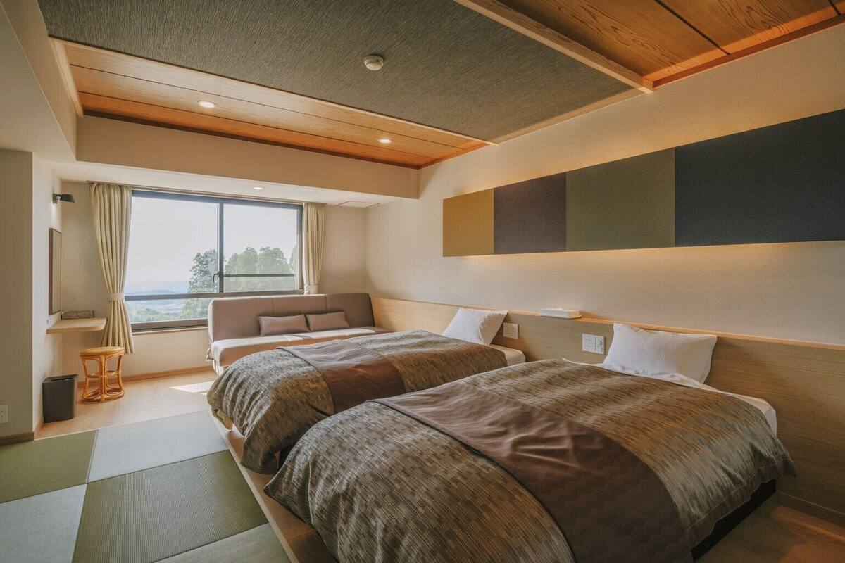 Habitación de hotel con dos camas, un ventanal grande, vistas al exterior y un diseño moderno.