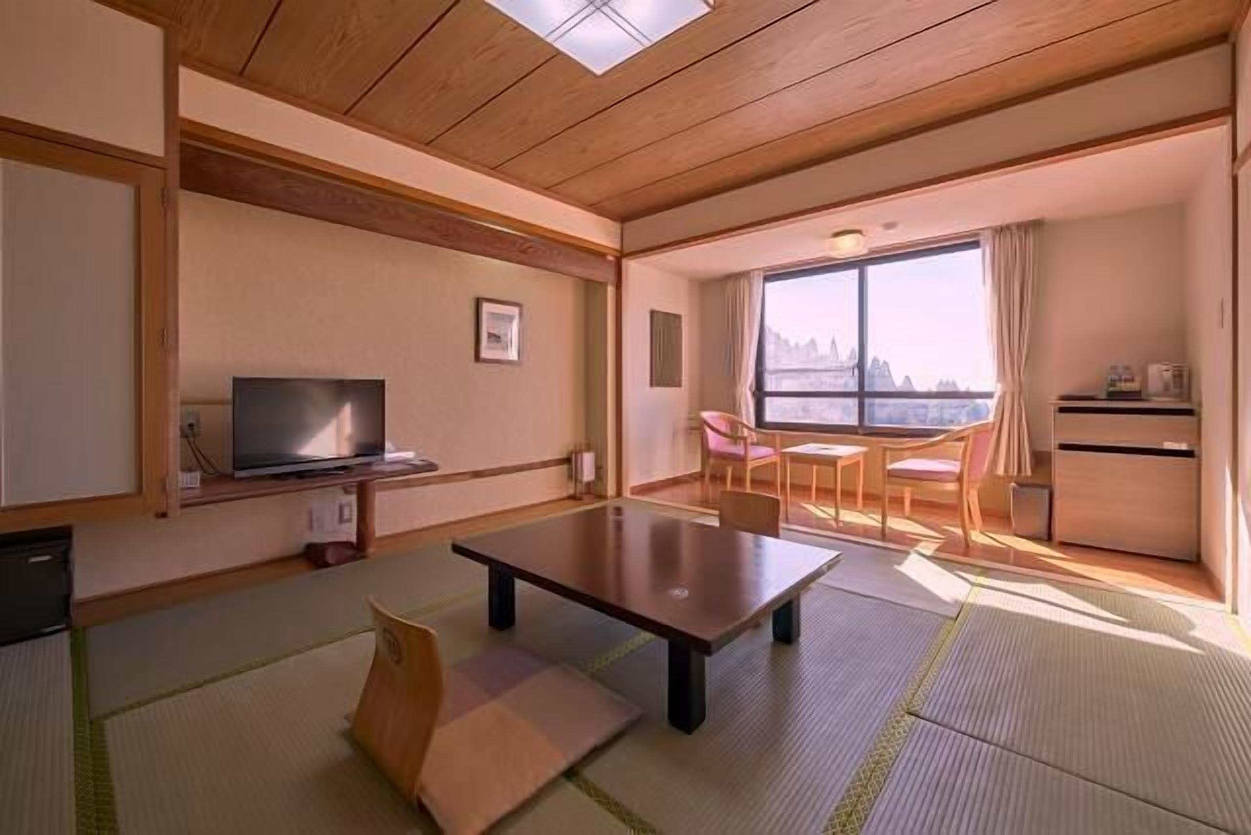Una habitación con televisión, una mesa, una silla, ventana con vistas y una kitchenette pequeña.