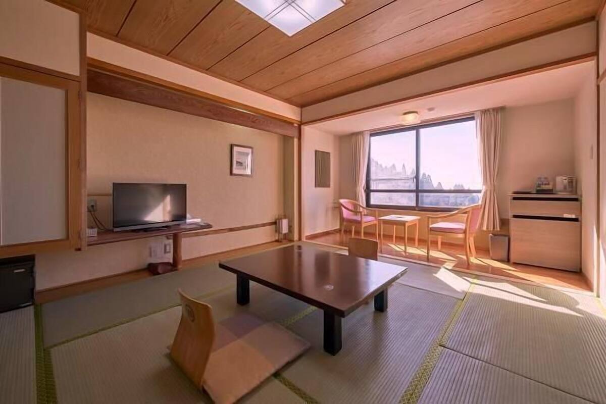 Una habitación con televisión, una mesa, una silla, ventana con vistas y una kitchenette pequeña.