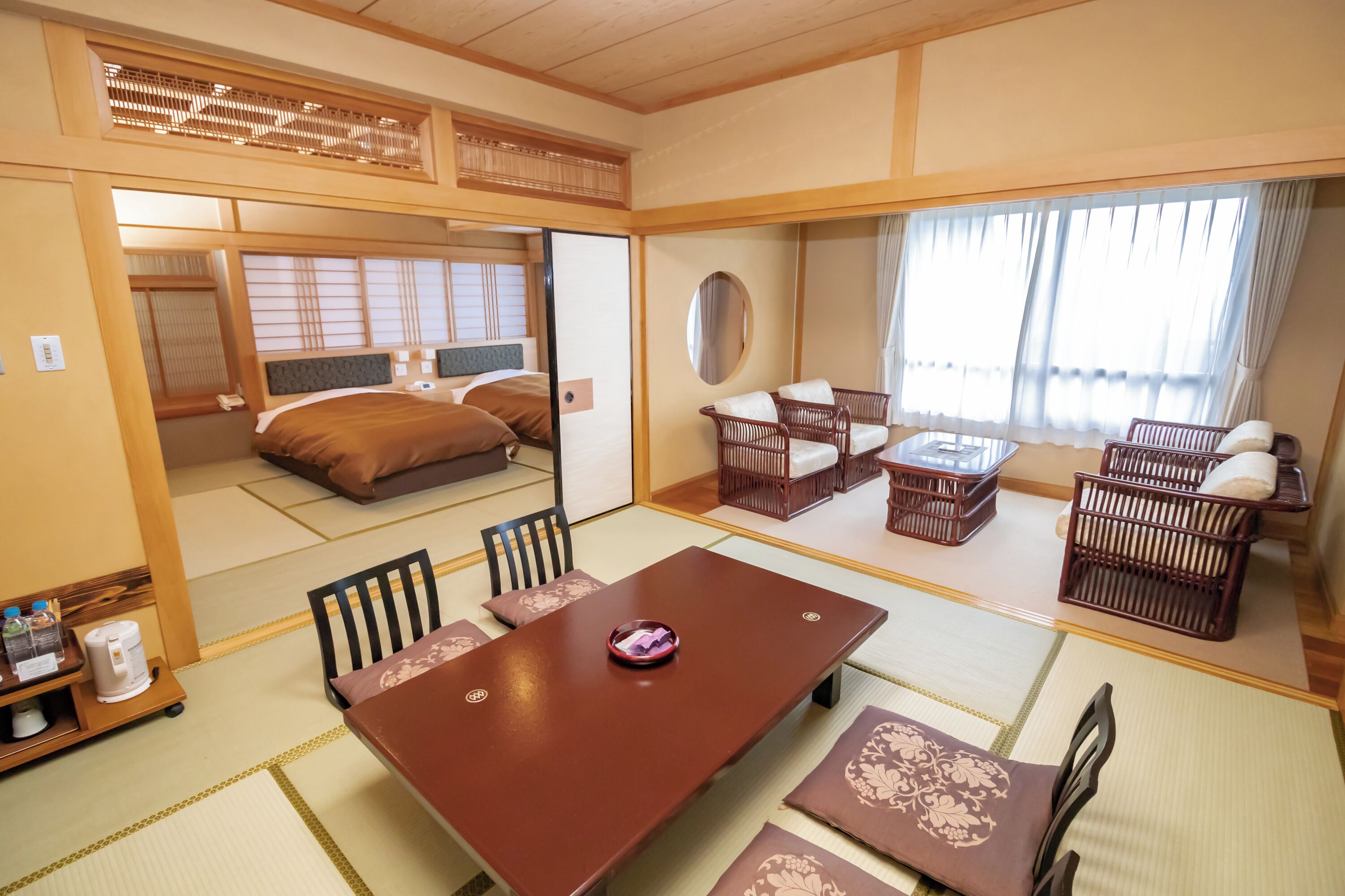 Una habitación de estilo japonés tradicional con suelo de tatami, una mesa baja con sillas, una cama con almohada y una puerta corredera.