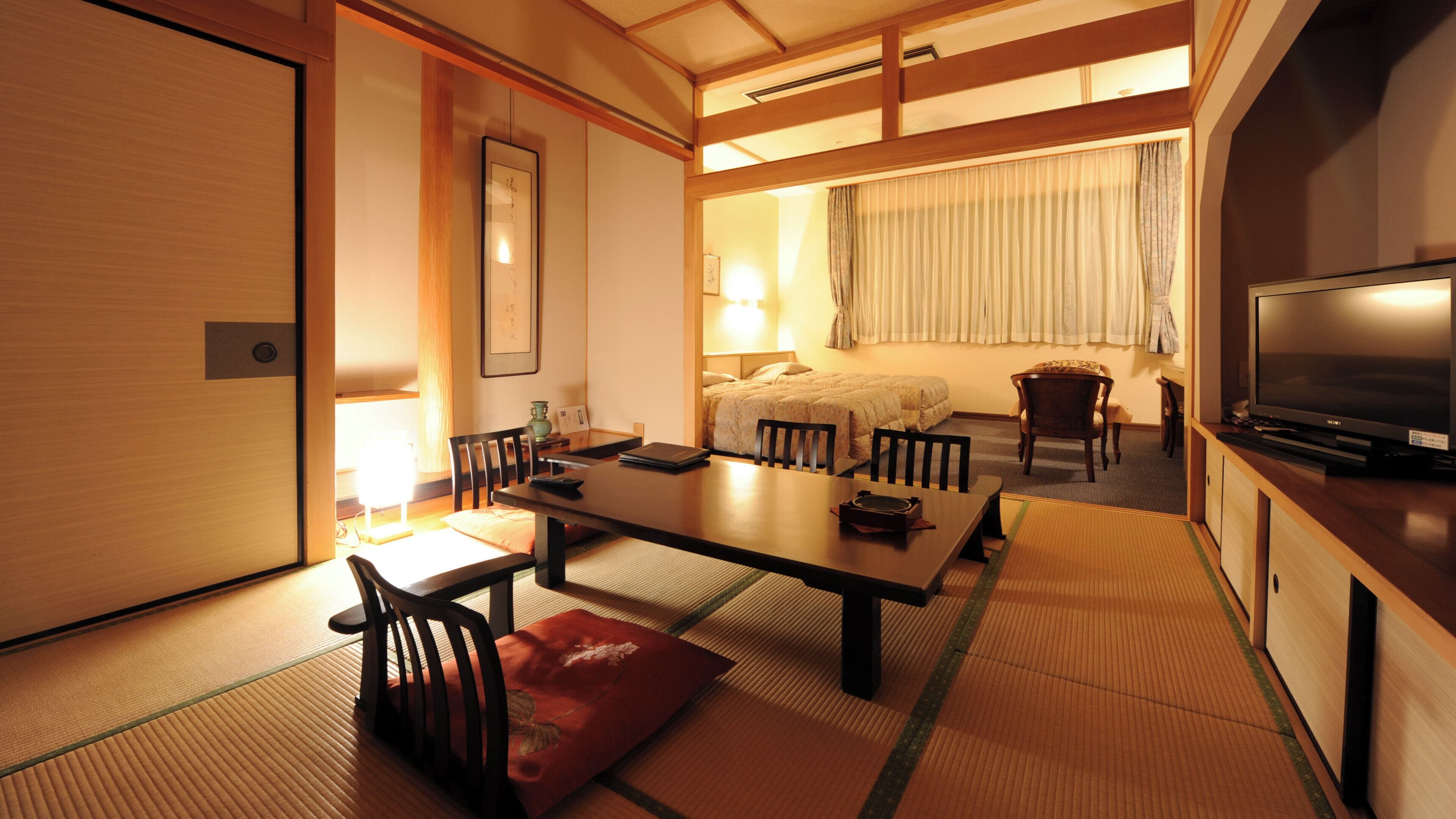 Una habitación tradicional japonesa con suelo de tatami, una mesa baja con sillas, una cama con dosel y un televisor sobre un soporte de madera.