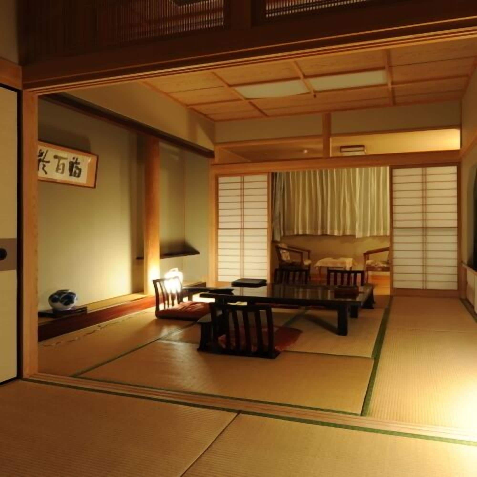 A traditional Japanese room with tatami flooring, a low table, chairs, a futon bed, and sliding doors.
