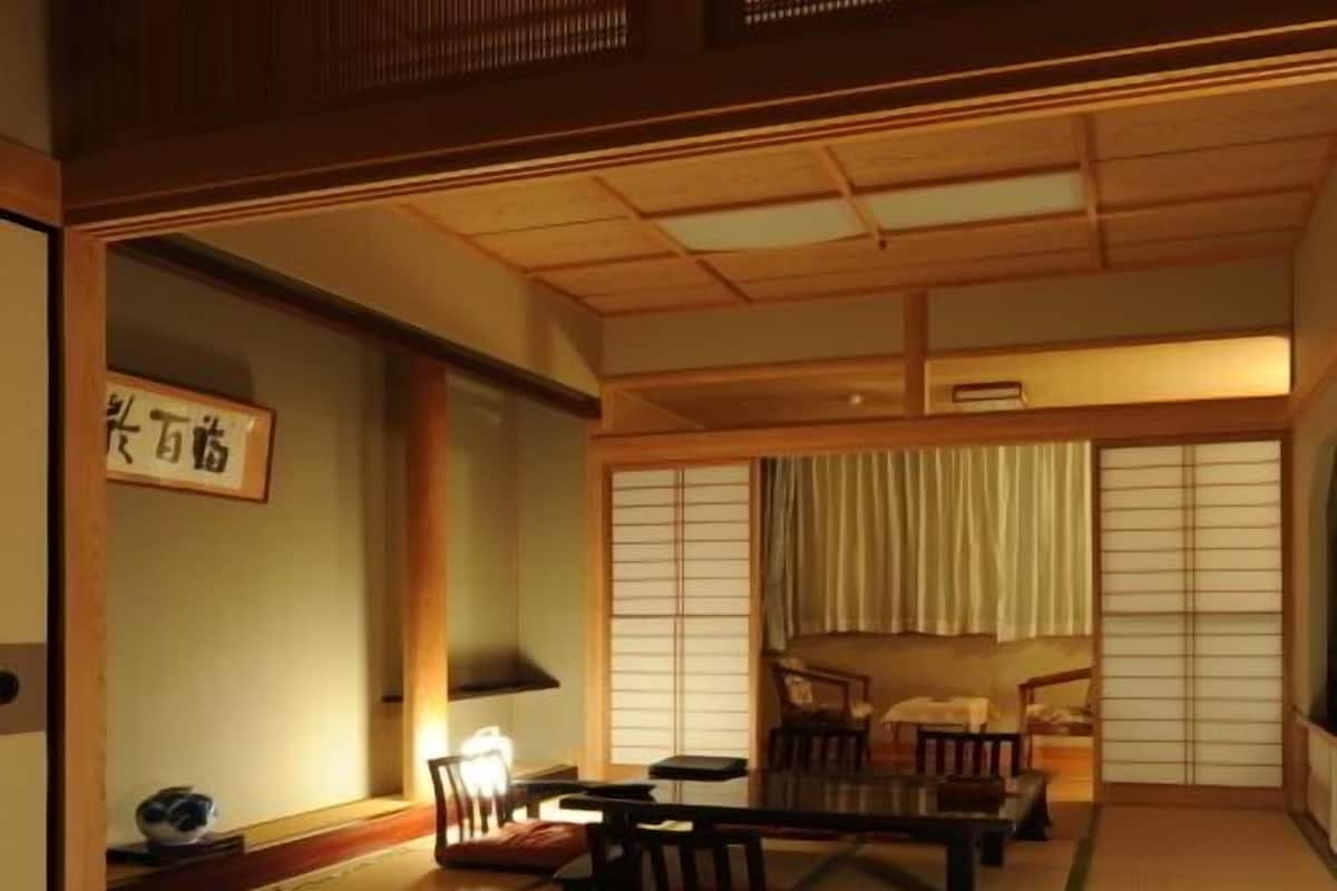 Una habitación japonesa tradicional con suelo de tatami, una mesa baja, sillas, un futón y puertas correderas.