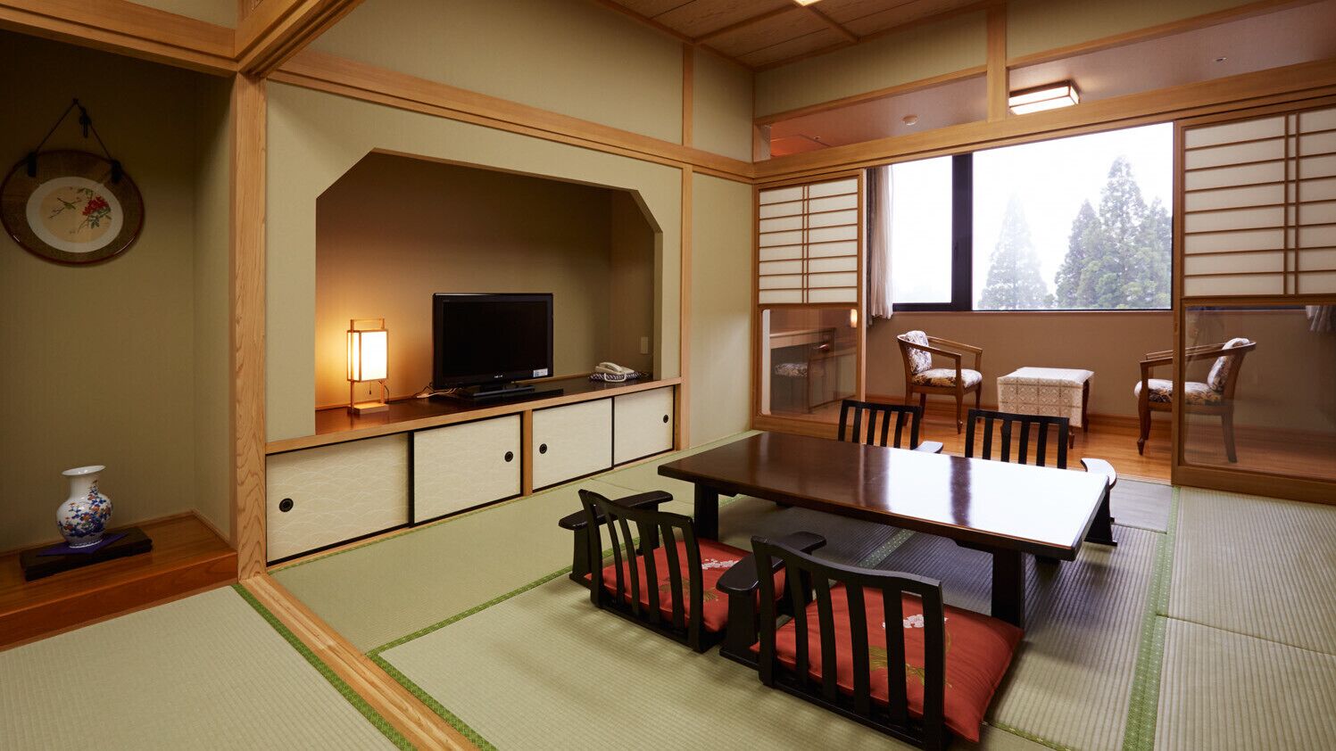 Una habitación japonesa tradicional con suelo de tatami, una mesa baja con sillas, un televisor y puertas correderas.