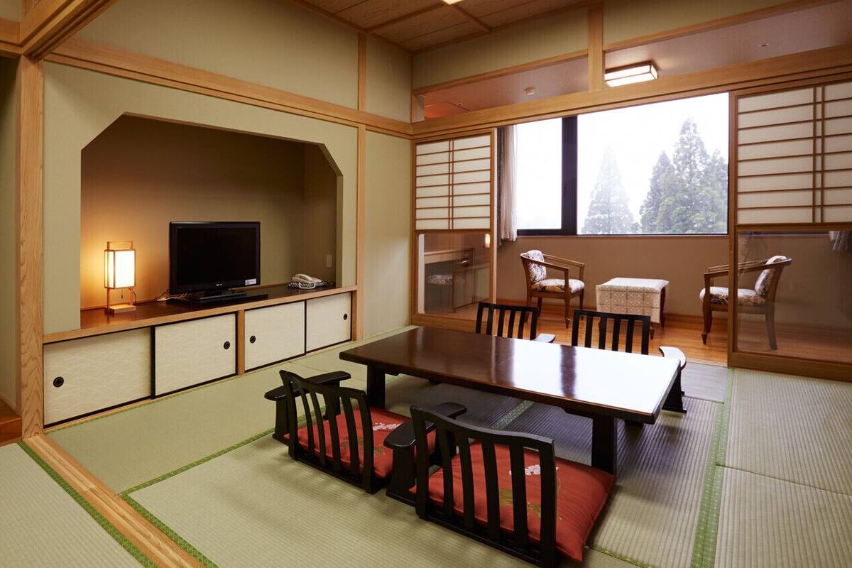 Una habitación japonesa tradicional con suelo de tatami, una mesa baja con sillas, un televisor y puertas correderas.