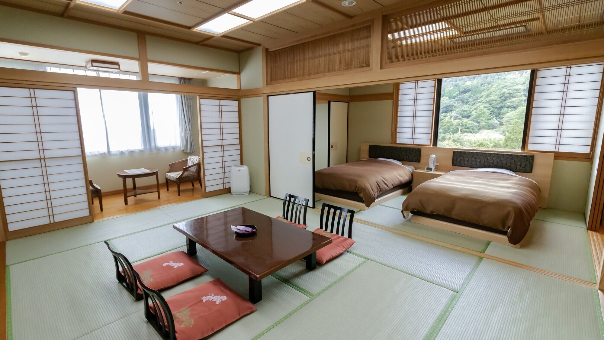 Una habitación japonesa tradicional con suelo de tatami, una mesa baja con cojines, una cama con cabecero y puertas correderas.