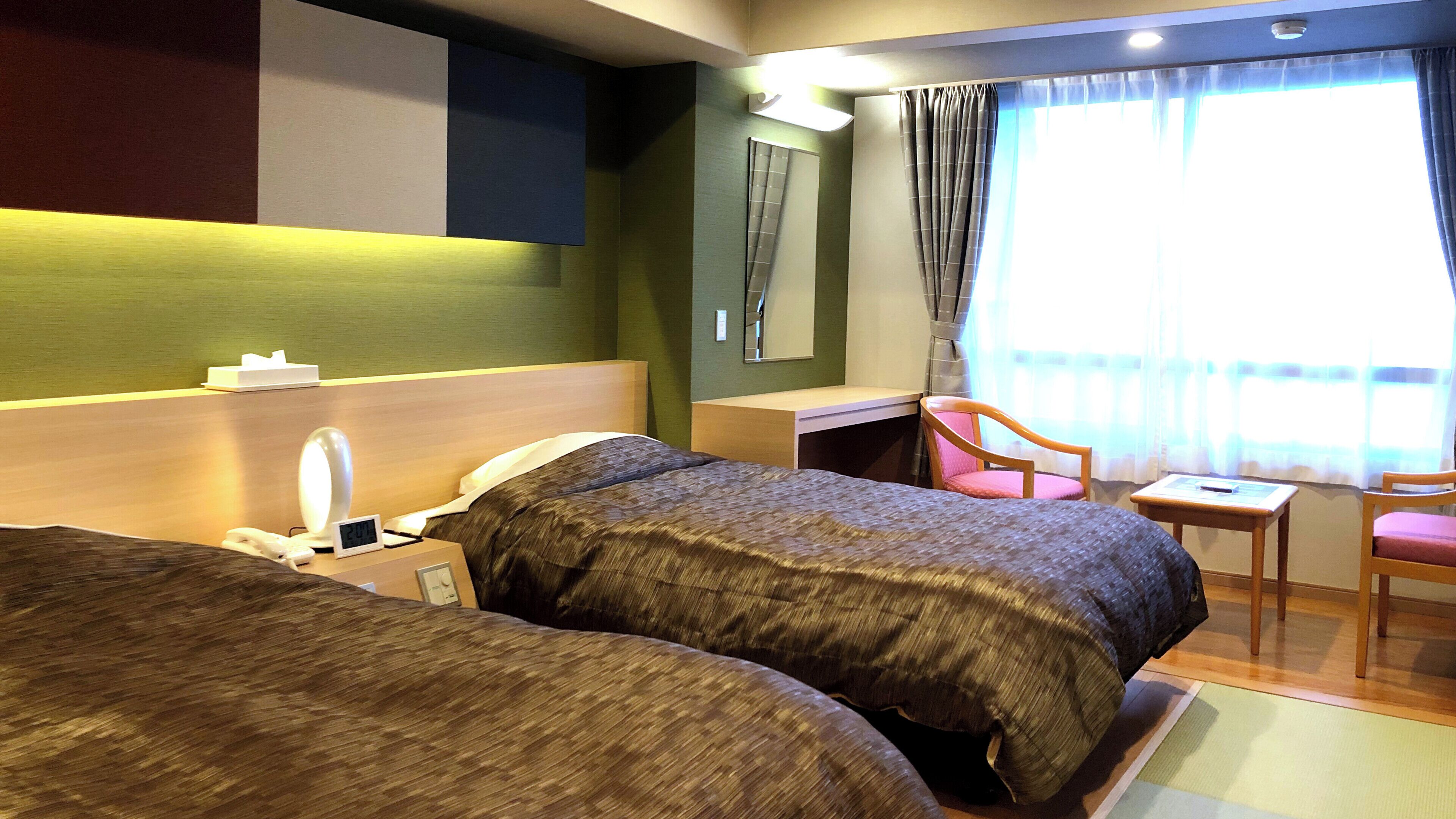 Habitación de hotel con dos camas, un escritorio, una silla, un espejo y una ventana con cortinas.