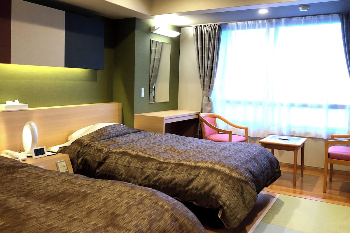 Habitación de hotel con dos camas, un escritorio, una silla, un espejo y una ventana con cortinas.