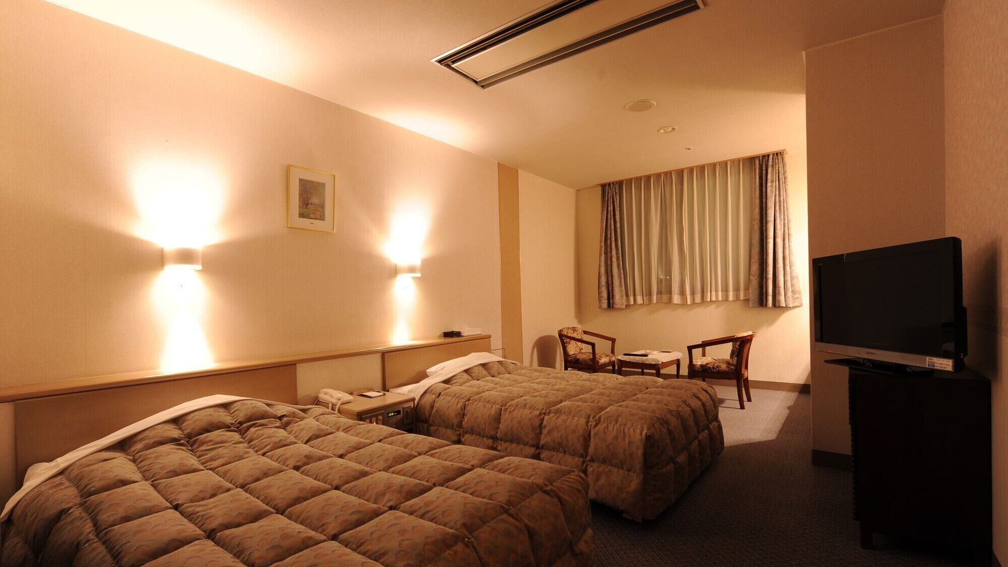 Habitación de hotel con dos camas, un escritorio, una silla, un televisor y un cuadro en la pared.