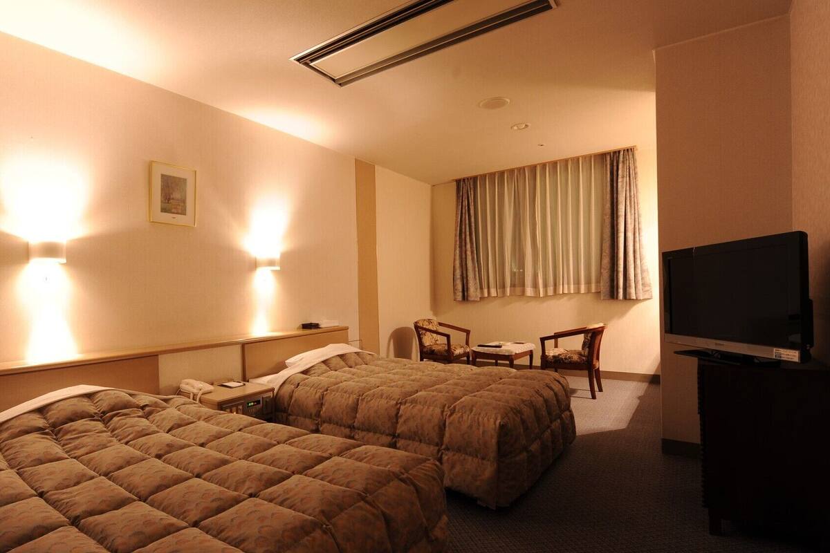 Habitación de hotel con dos camas, un escritorio, una silla, un televisor y un cuadro en la pared.