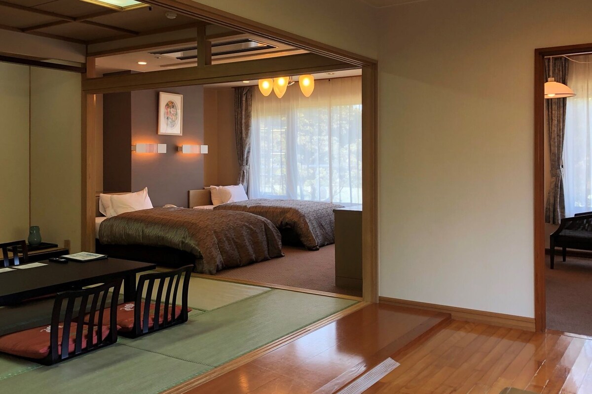 Ein traditioneller japanischer Raum mit Tatami-Boden, einem niedrigen Tisch mit Kissen und einem Bett mit Futon.
