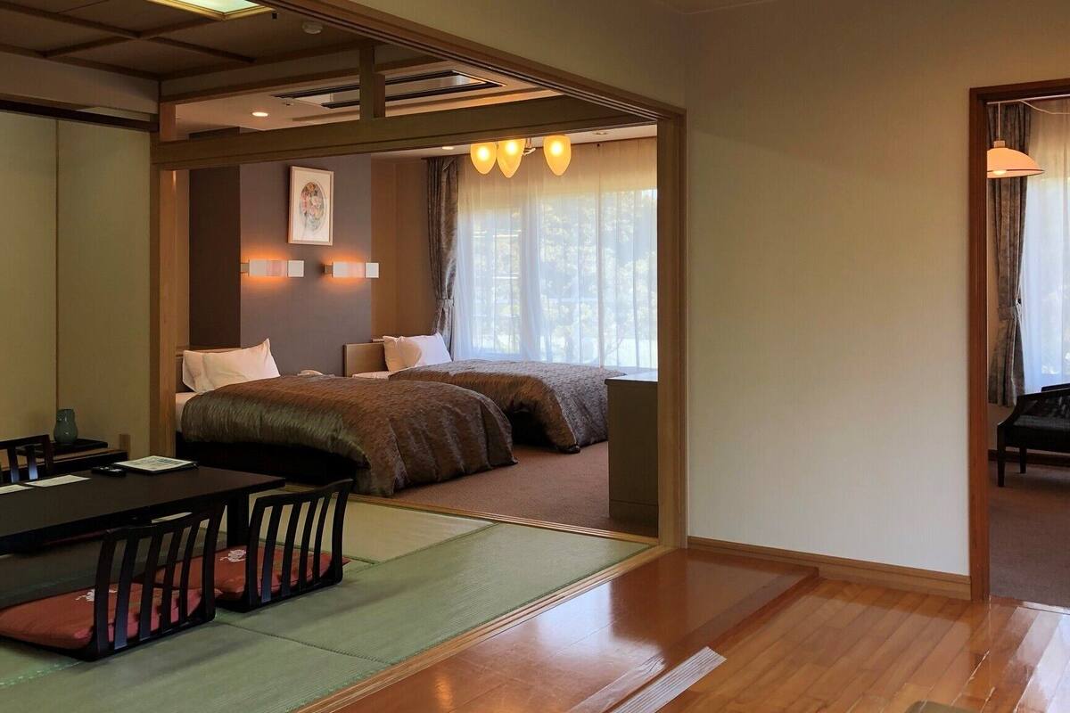 Una habitación tradicional japonesa con suelo de tatami, una mesa baja con cojines y una cama con futón.