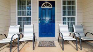 A front porch with a blue door, two white chairs, and a welcome mat. - Creekside Stay Near Fort Benning Sleeps 12! (Columbus)