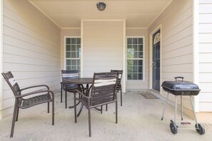 Un patio techado con mesa y sillas, una parrilla y una puerta.
