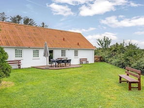 A white house with a red roof, a patio with a table and chairs, and a grassy yard. - 4 Star Holiday Home in Lokken (Lokken)