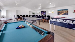 Un vaste espace de loisirs intérieur comprenant une table de billard, un baby-foot et une table de jeu de flipper.