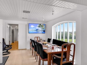 Ein Essbereich mit einem Holztisch, Stühlen und einem großen Fenster mit Blick auf Grünflächen.