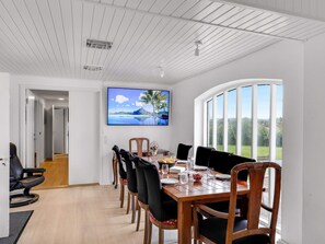 A dining area with a wooden table, chairs, and a television mounted on the wall displaying a scenic image. - 4 Star Holiday Home in Lokken (Lokken)