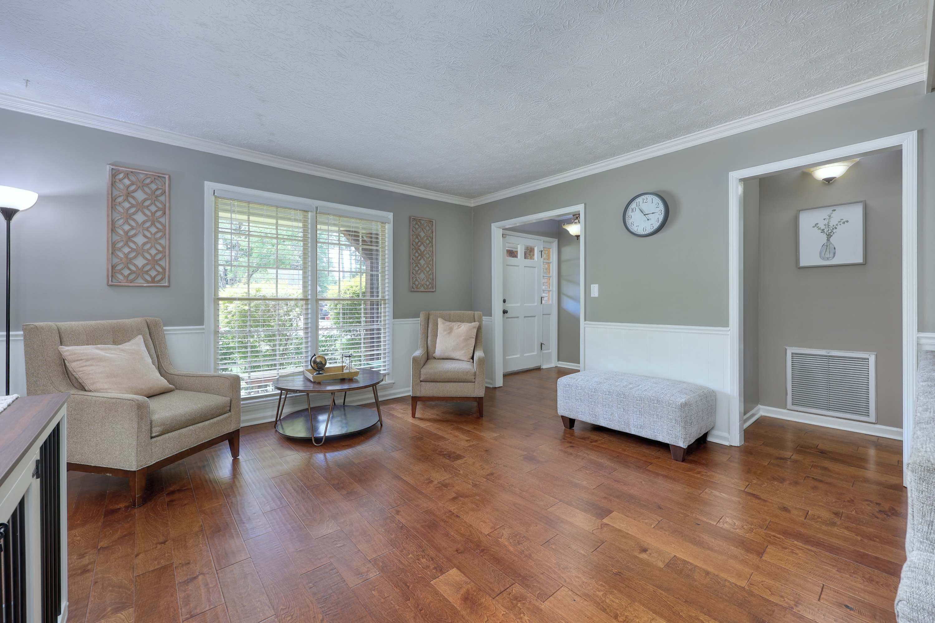 A spacious living room with hardwood flooring, a beige armchair, a round coffee table, and a white bench.
