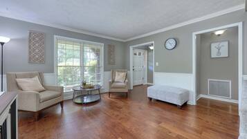 A spacious living room with hardwood flooring, a beige armchair, a round coffee table, and a white bench.