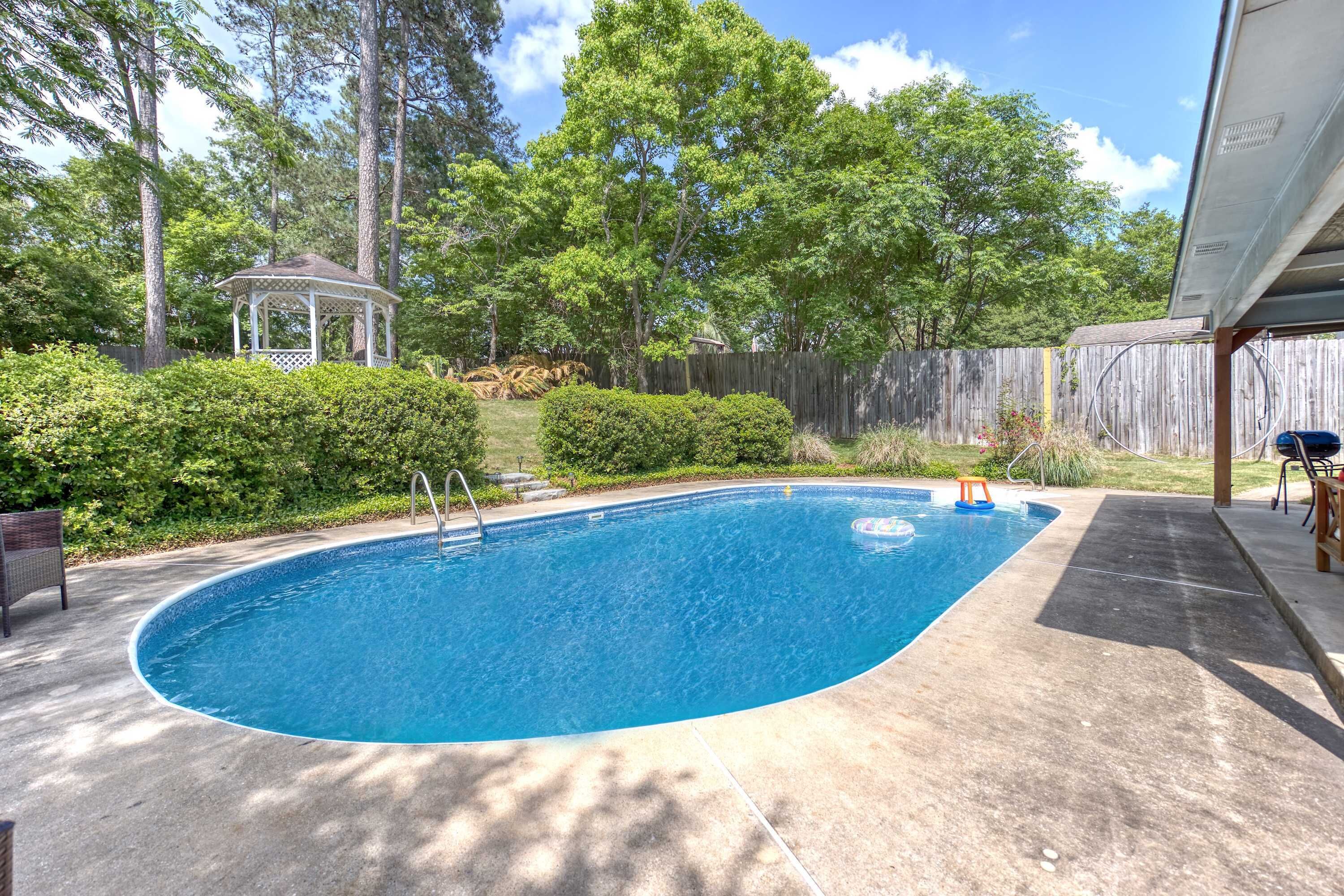 A backyard with a swimming pool, a gazebo, and a wooden fence.
