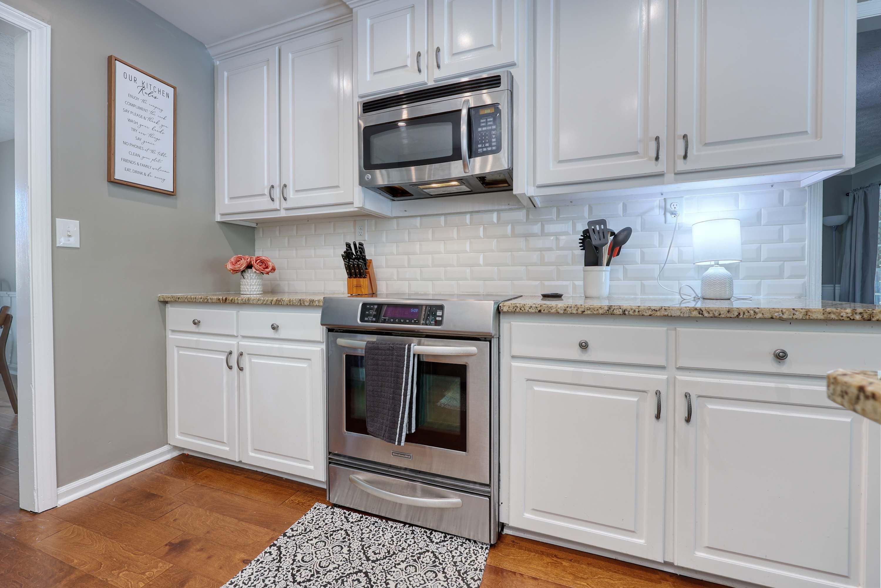 A kitchen with white cabinets, a stainless steel microwave, and an oven.