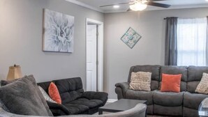 A living room with a gray sofa, a black armchair, a coffee table, and a ceiling fan. - Historic Edgewood Home: Modern Charm, (Columbus)