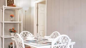 A dining area with a glass-top table, white chairs, and a white shelving unit with decorative items. - Historic Edgewood Home: Modern Charm, (Columbus)